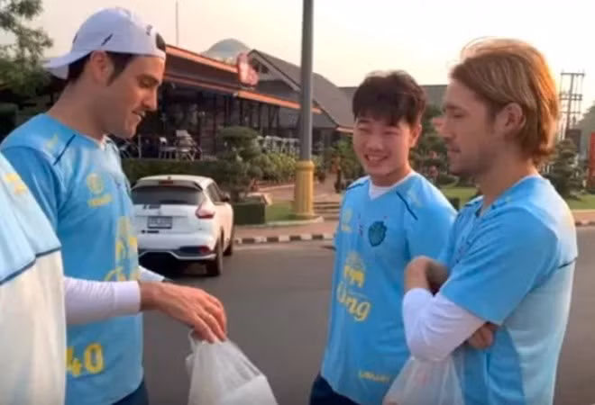 Tiền vệ Lương Xuân Trường thoải mái ngồi lề đường ăn cơm nắm và thịt xiên cùng các đồng đội.