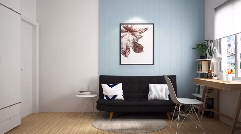 Phòng làm việc nhẹ nhàng, yên tĩnh với bàn gỗ đặt gần cửa sổ, ghế sofa màu xám đen đặt dưới bức tường màu xanh.