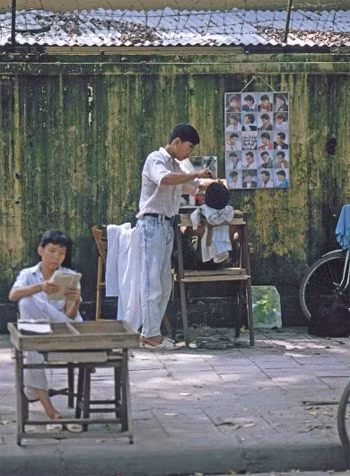 Tiệm cắt tóc vỉa hè chắc chắn sẽ là cả một trời kí ức với những người Hà Nội xưa. Chẳng cầu kì, điều hòa hay Wifi mà thay vào đó là chiếc gương nhỏ, cái ghế gỗ và một chiếc khăn choàng còn dính đầy tóc của người cắt trước đó.