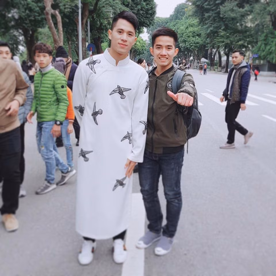 Đình Trọng cùng Văn Quyết diện áo dài với quần jeans phóng khoáng. Mẫu áo đính kết cánh chim én, vẹt rực rỡ sắc màu nổi bật trên nền màu kem nhạt, chất liệu thô đũi khỏe khoắn, năng động đúng với tính chất của những cầu thủ.