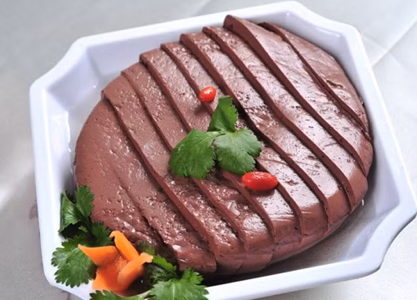 2. Tiết lợn sốt mỡ hành. Nguyên liệu: Tiết lợn đã luộc, hành lá, tỏi, ớt, chanh, nước mắm. Tiết lợn đã luộc cắt thành miếng vuông. Bắt nồi nước bỏ tiết vào hấp chín. Hành lá rửa sạch, cắt nhỏ. Ảnh: matongthiennhien.vn.
