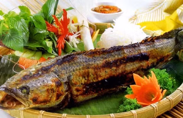 4. Cá lóc nướng lá chuối. Nguyên liệu: Cá lóc, lá chuối, gia vị, giấy bạc. Cá lóc sơ chế sạch nhớt, ướp cá cùng với muối, đường, tiêu, mật ong và dầu hào. Bọc cá vào trong lá chuối, buộc chắt 2 đầu lại rồi bọc thêm 1 lớp giấy bạc bên ngoài và đem nướng cá trên than hồng khoảng 30 phút là cá chín thơm nức. Ảnh: cakhohanam.org.