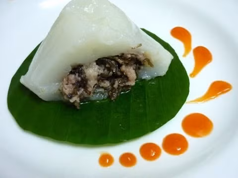 Cho nước dùng vào tô bột đã trộn và khuấy đều để có phần bột dẻo. Gấp lá chuối thành hình phễu, trát đều bột quanh phễu lá chuối, sau đó cho nhân vào giữa và cuối cùng cho phần bột lên trên cùng, kín hết phần nhân. Gấp mép lá thành hình tam giác và gói kín. Đem bánh đi luộc với nước ngập mặt bánh và nấu với lửa nhỏ trong khoảng 20 phút. Ảnh: Youtube.com.