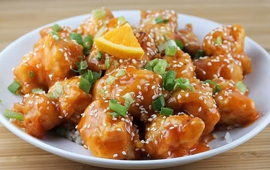 Vẫn dùng chảo rán gà, đổ bớt lượng dầu thừa. Phi nửa phần vỏ cam đã bào và tỏi, sau đó đổ nước cam, chế thêm nước mắm. Đợi đến khi hỗn hợp sôi lên thì cho gà vào, để lửa nhỏ, om đến khi nước đặc sệt lại là được. Đổ gà ra đĩa. Cho hành lá và chút vừng trắng lên để trang trí. Ảnh: toinayangi.vn.