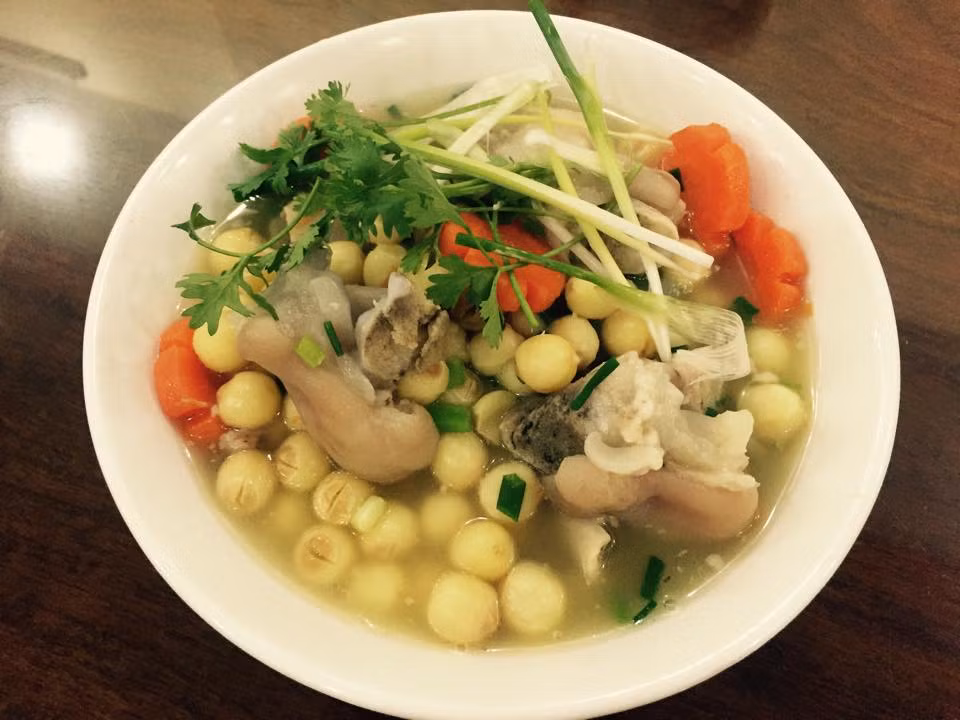 1. Chân giò hầm hạt sen. Nguyên liệu: Chân giò nguyên xương, hạt sen, cà rốt, hành tây, nấm hương, hành, mùi tàu. Chân giò cạo thật sạch lông rồi ướp với hạt nêm, gia vị, hành khô băm nhỏ rồi cất vào tủ lạnh khoảng 2 giờ cho ngấm. Hạt sen, nấm hương ngâm nở. Ninh nhỏ lửa để hạt sen chín bở mà vẫn ko bị nát, để riêng. Đổ nước sâm sấp mặt thịt rồi ninh trong nồi áp suất sôi khoảng 20 phút thì tắt bếp. Xem thịt đã nhừ chưa, có thể xiên đũa qua dễ dàng thì trút hạt sen, nấm hương vào đun cùng, nêm nếm lại cho vừa miệng. Hành tây bổ múi cau, cà rốt tỉa hoa xắt mỏng, hành mùi tàu thái nhỏ đợi chuẩn bị bắc thịt xuống thì trút vào nồi. Ảnh: bepgiadinh.com.