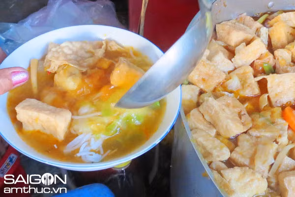 Bắt nước lên bếp nấu sôi cho cà rốt và khoai tây, đậu vô ve, bí vào nấu chín. Phi dầu ăn với boa rô vàng đều, cho cà chua vào tạo màu, cho nấm rơm,thơm, đậu khuôn vào xào chung với măng chua, nêm chút muối, chút đường, xì dầu, tiêu, xào cho thấm gia vị. Ảnh: nethue.com.vn.