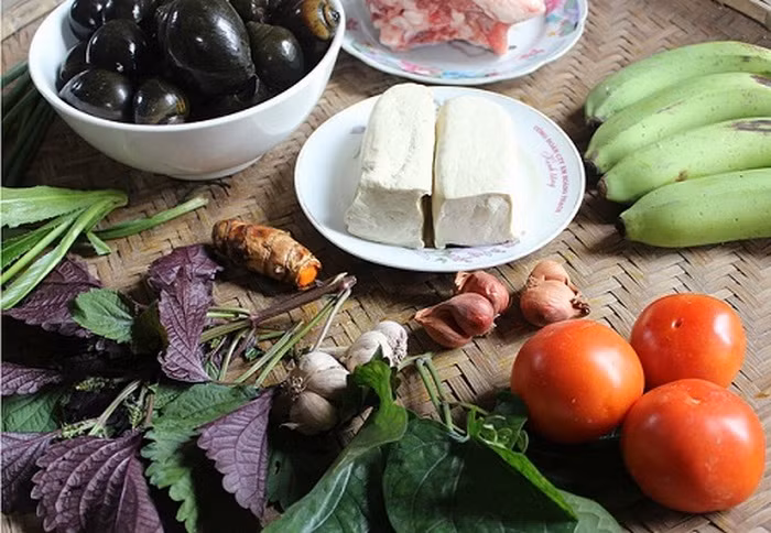 Ốc om chuối đậu. Nguyên liệu gồm ốc nhồi, thịt ba chỉ cắt miếng vừa ăn, đậu phụ rán, chuối xanh thái lát ngâm muối, giấm bỗng. Bột nghệ, tía tô, lá lốt, hành hoa, hành khô, dầu ăn, gia vị, muối trắng, ớt tươi theo khẩu vị gia đình. Ốc nhồi mua về rửa sạch và luộc, khêu thịt ốc, cắt bớt phần đít và rửa sạch, nước luộc chắt riêng. Ảnh: Lamsao.