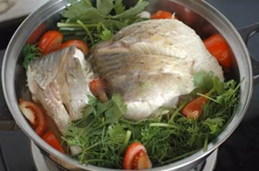 Quả dọc nướng qua lửa bổ đôi cho vào nồi cá hấp cùng với cà chua, tiếp tục đun nhỏ lửa để cá được ngấm gia vị. Khi cá vược hấp bia chín chỉ việc cho hành hoa, thì là, cần tây lên trên đun thêm 3 phút nữa thêm mì chính rồi cho cá ra đĩa. Ảnh: Tinmoi.vn.