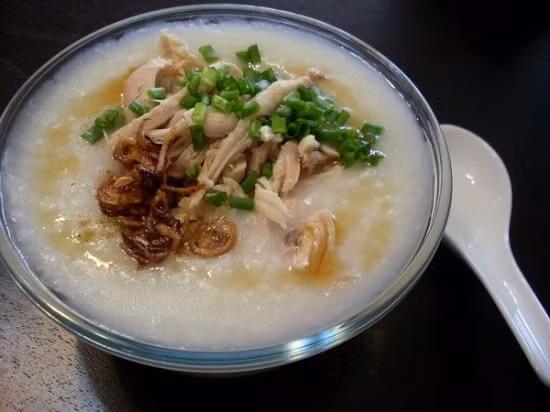Mẹ chuẩn bị gạo, thịt gà tươi, hành và những loại gia vị thông thường. Gà luộc chín, vớt ra để nguội rồi xé nhỏ. Vo gạo, thêm nước luộc gà rồi ninh cho nhừ. Cháo chín, cho thịt gà vào ninh nhừ. Thêm gia vị, tắt bếp và múc ra bát, thêm hành lá. Ảnh: toinayangi.vn.