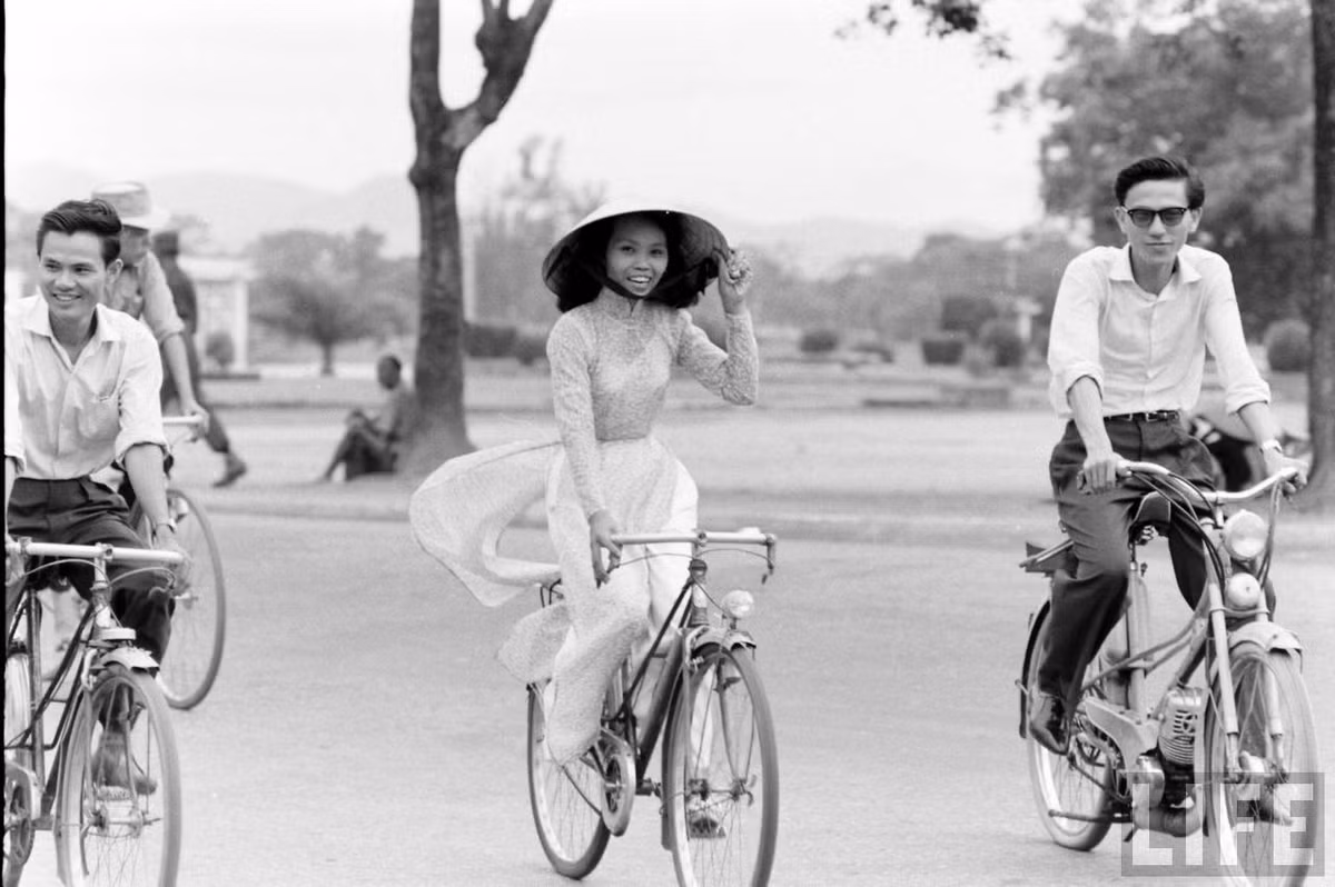 Thiếu nữ áo dài Huế tươi tắn khi đạp xe bên các đấng mày râu, 1961. Ảnh: Life.