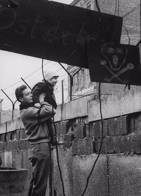 Người đàn ông bế con hướng tầm mắt nhìn sang phía bên kia của Bức tường Berlin năm 1961.