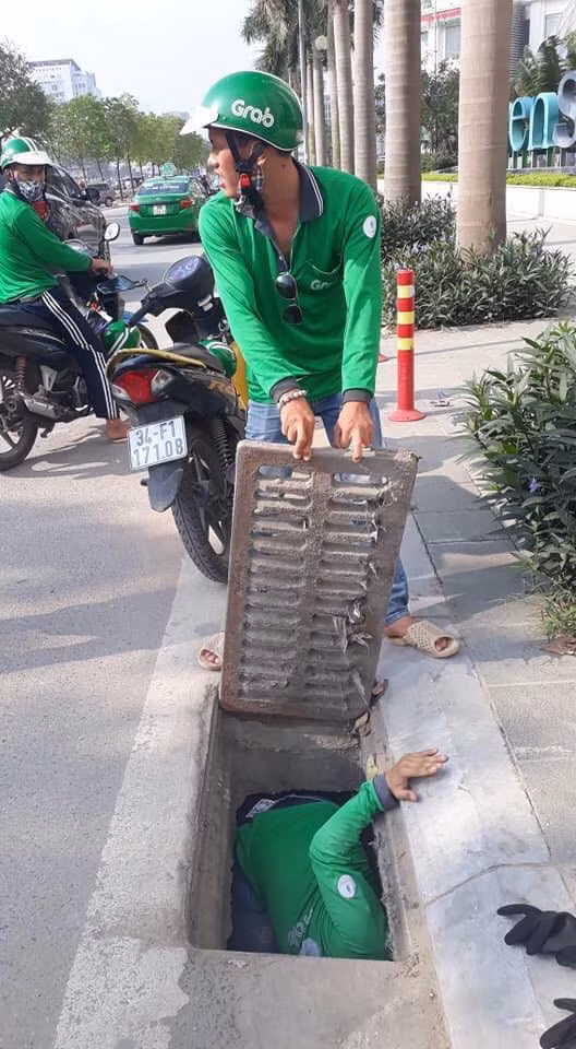 Hai tài xế GrabBike cùng nhau giúp vị khách nước ngoài nhặt thẻ ngân hàng bị đánh rơi dưới cống nước ở Hà Nội sáng 8/5. Ảnh: ALBANY OWENS.