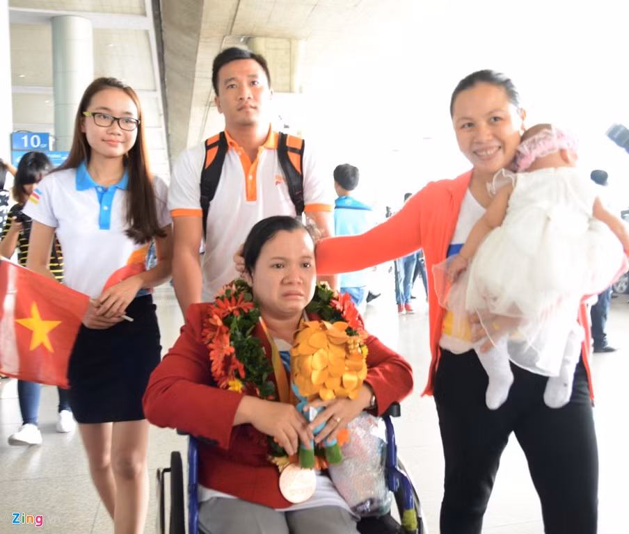 VĐV Đặng Thị Linh Phượng bật khóc khi về đến Việt Nam. Tại giải đấu vừa qua, cô đã giành HCĐ hạng cân dưới 50 kg nữ ở môn cử tạ. Vợ của Lê Văn Công, chị Chu Thị Tám vừa bế con vừa an ủi đồng nghiệp của chồng.