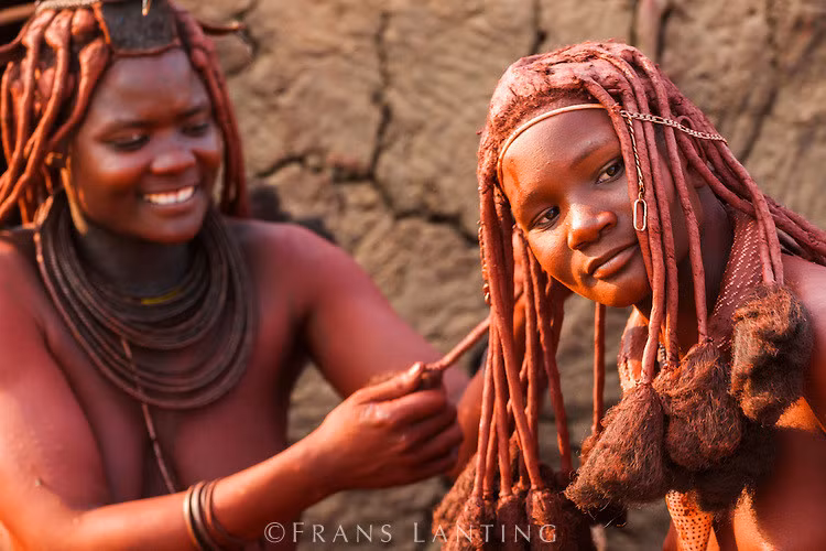 Bộ tộc Himba, Namibia: Phụ nữ của tộc Himba nổi tiếng với tóc và làn da ánh đỏ. Họ bôi otjize - một hỗn hợp gồm bơ, mỡ và đất đỏ - lên tóc và da hàng ngày. Nhiều người cho rằng otjize giúp tránh nắng và chống côn trùng, nhưng tộc Himba cho biết họ dùng chúng chỉ hoàn toàn vì lý do thẩm mỹ. Ảnh: Frans Lanting.