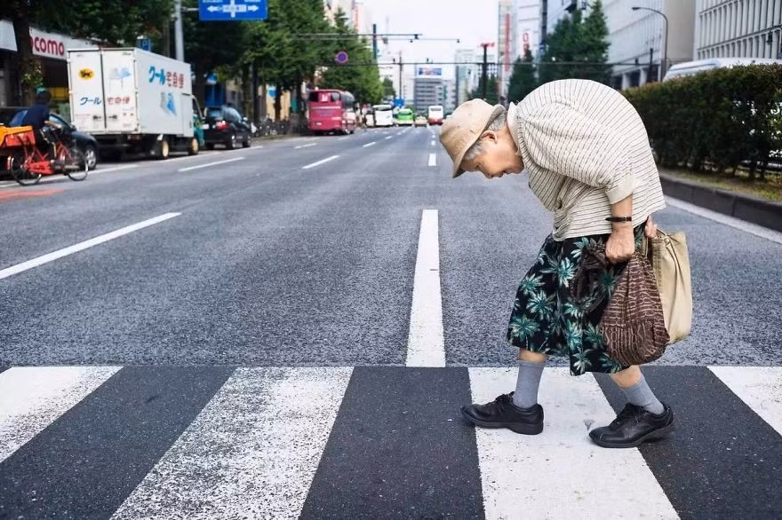 Một bà cụ còng lưng khó khăn bước qua đường.