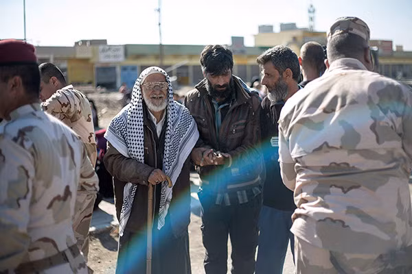 Binh sĩ quân đội Iraq đỡ một cụ già qua chốt kiểm soát trên một con đường ở phía đông Mosul.