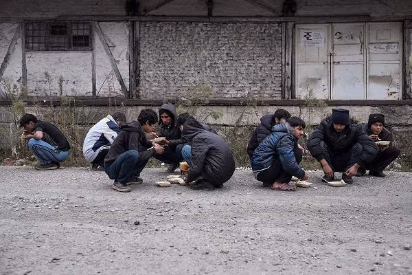 Những người tị nạn ngồi túm tụm ăn trưa gần một nhà kho bỏ hoang ở Serbia.