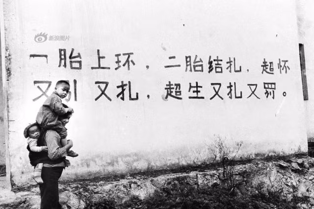 Bức ảnh chụp tại Quý Châu năm 1996. Trên tường là một khẩu hiệu với nội dung: “Sau khi sinh con đầu lòng thì đặt vòng tránh thai, sinh con thứ hai đi thắt ống. Nếu sinh quá quy định sẽ phải phá thai và phạt”.