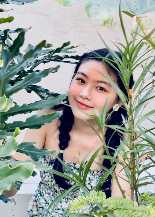 Lọ Lem diện đầm xanh, tóc tết 2 bên khoe sắc trong khu vườn trên sân thượng tại nhà.