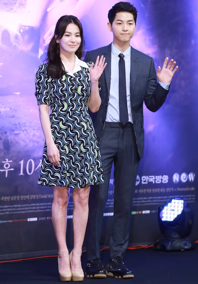 Vì chiều cao “khiêm tốn”, Song Hye Kyo luôn mang giày cao gót dáng trơn, phối với đầm chít eo có họa tiết độc đáo. Bộ đầm “nhuộm” sắc xanh trầm của cô khá hợp tông với trang phục của Song Joong Ki.