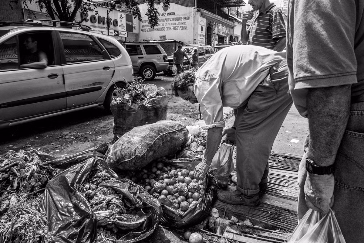 Người đàn ông lớn tuổi đang bới túi đựng cà chua và khoai tây do một người bán hàng rau bỏ lại vào cuối ngày. Lạm phát đã khiến thực phẩm ở nước này tăng giá. Một túi cà chua dễ dàng bằng cả một ngày lương.
