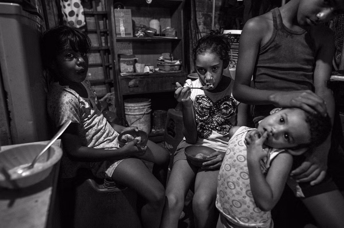Hiện nay, mối lo lớn nhất của dân Venezuela chính là tình trạng thiếu lương thực, thực phẩm và thuốc men. Mỗi ngày, hàng nghìn người đứng xếp hàng dài bên ngoài các siêu thị hay cửa hàng từ lúc trời tờ mờ sáng để mua một vài thứ nhu yếu phẩm như gạo hay lúa mì với giá thấp hơn ngoài thị trường. Ảnh: Bốn em nhỏ ăn chuối trong căn bếp ở nhà.