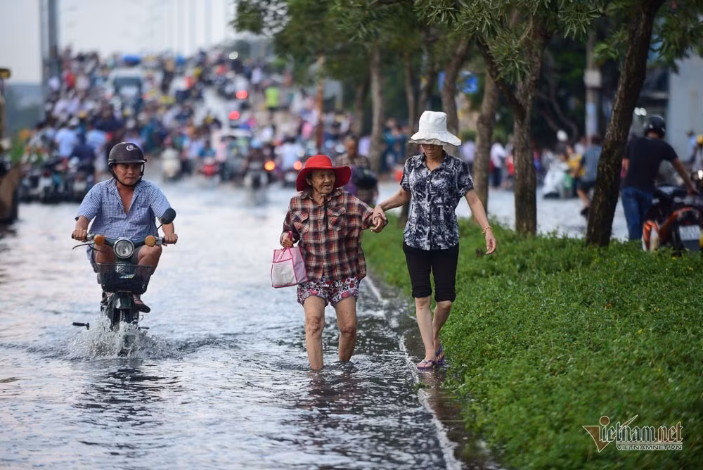 Một cụ già phải nhờ hỗ trợ khi di chuyển qua đoạn đường ngập.