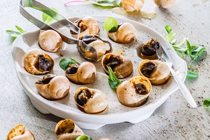 Do dùng cả vỏ để trình bày món ốc sên nên đầu bếp cũng phải làm sạch chúng một cách cẩn thận. Tại một số quốc gia, vỏ ốc sên được thay thế bởi những chiếc bánh ngọt nhỏ nhiều lớp (puff pastry). Như vậy trông món ăn vệ sinh hơn nhưng bánh ngọt lại ngấm bơ và làm mất sự thú vị khi thưởng thức ốc sên. Ảnh: Vivial.