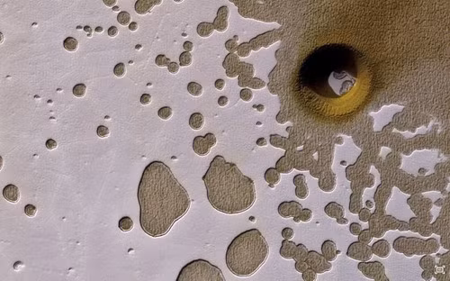 Tàu thăm dò sao Hỏa Mars (MRO) của NASA chụp ảnh hố lõm kỳ lạ trên sao Hỏa. Xung quanh miệng hố toàn băng và bụi. Khí Co2 lạnh phủ đầy miệng hố, phản ứng hóa học với các vật chất tạo ra một gam màu vàng pho mát độc lạ. Nguồn ảnh: Dailymail.