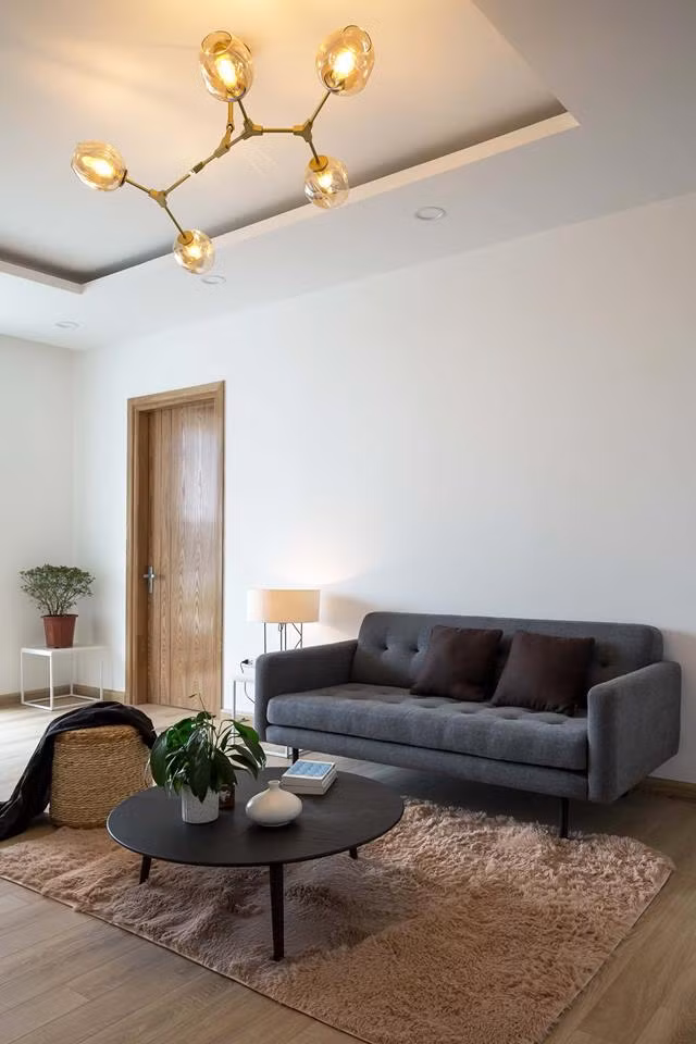 Phòng khách giản dị với sofa đơn, bàn trà tròn, thảm trải sàn và ghế ngồi làm thủ công.