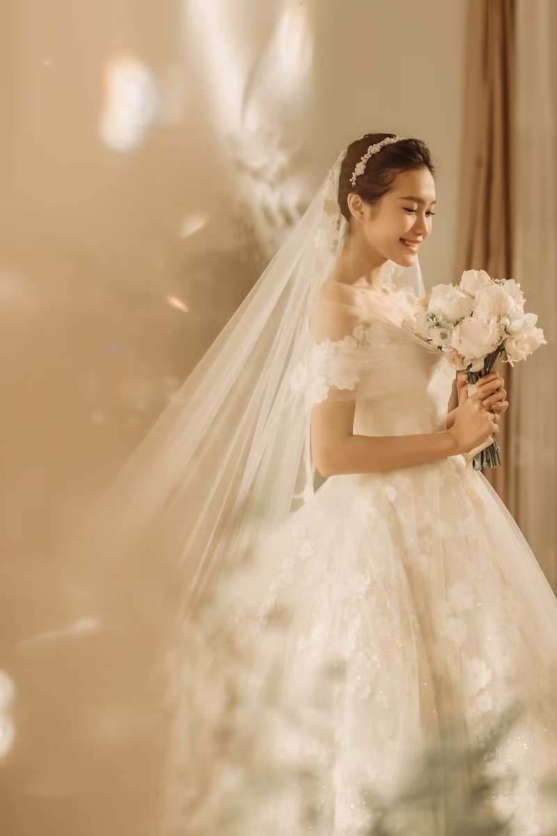 Bộ váy phủ ren với những bông hoa ngọt ngào yêu kiều, cộng thêm khăn voan mềm mại, nhìn cô dâu gốc Hà Nội càng thêm e ấp, duyên dáng tựa nàng công chúa bước ra từ truyện cổ tích để sánh bước cùng chàng hoàng tử của cuộc đời.