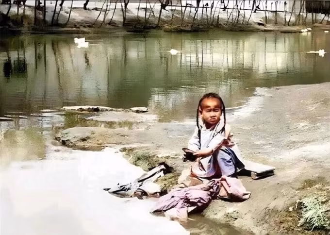 Một bé trai nhỏ tuổi phụ giúp gia đình giặt quần áo bên bờ sông.