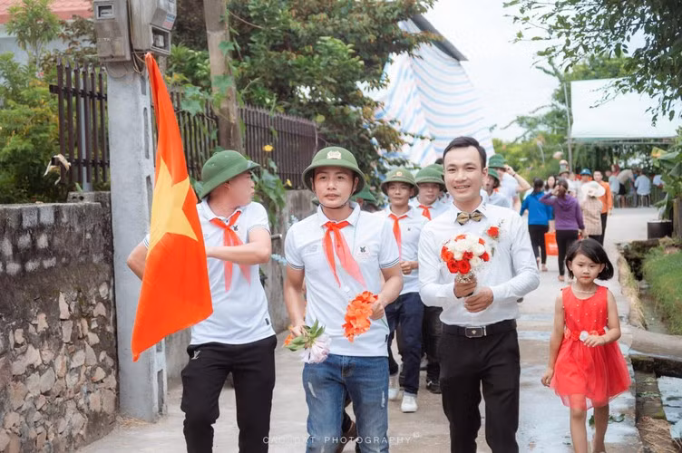 Thay vì diện trang phục bảnh bao như thường lệ thì dàn khách mời nhà trai lại diện đồng phục mũ cối, quàng khăn đỏ và người dẫn đoàn còn cầm theo cờ Tổ quốc.