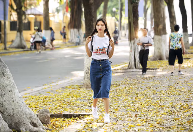 Cô gái trẻ khoe nét xuân thì trên con đường ngợp đầy lá vàng.