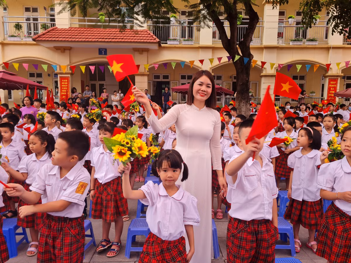 Cô giáo tươi cười vẫy cờ hoa cùng các học sinh đón chào một năm học nhiều niềm vui.