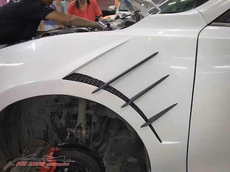 Bản độ Mazda 3 này cũng đã được Phi Long chỉnh sửa lại khá nhiều ở hai bên thân xe. Trong đó, các vè trước của chiếc xe nay đã được "trổ" thêm những khe tản nhiệt như nhiều mẫu xe thể thao "hàng khủng". Bên cạnh đó, bản lề cửa trước nguyên bản của Mazda 3 cũng đã được thay thế.