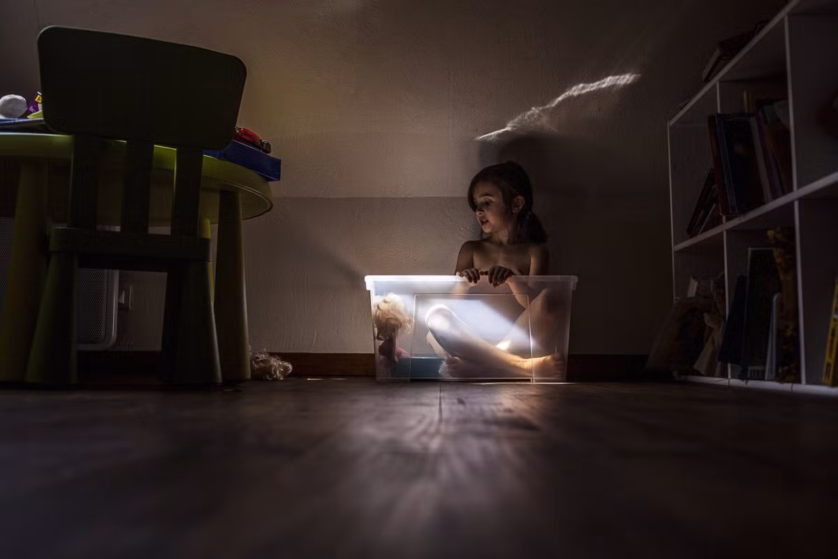 Bé gái chơi cùng búp bê trong hộp nhựa.