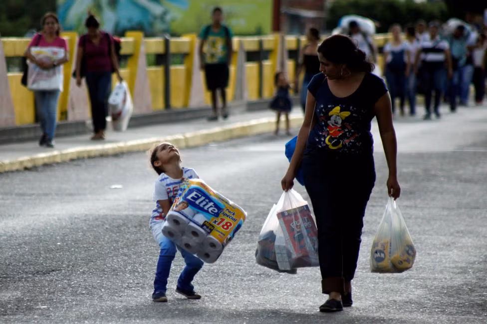 Một em nhỏ Venezuela mang túi giấy vệ sinh cạnh một phụ nữ cũng xách theo nhiều đồ khi đi qua biên giới Colombia-Venezuela ngày 10/7.