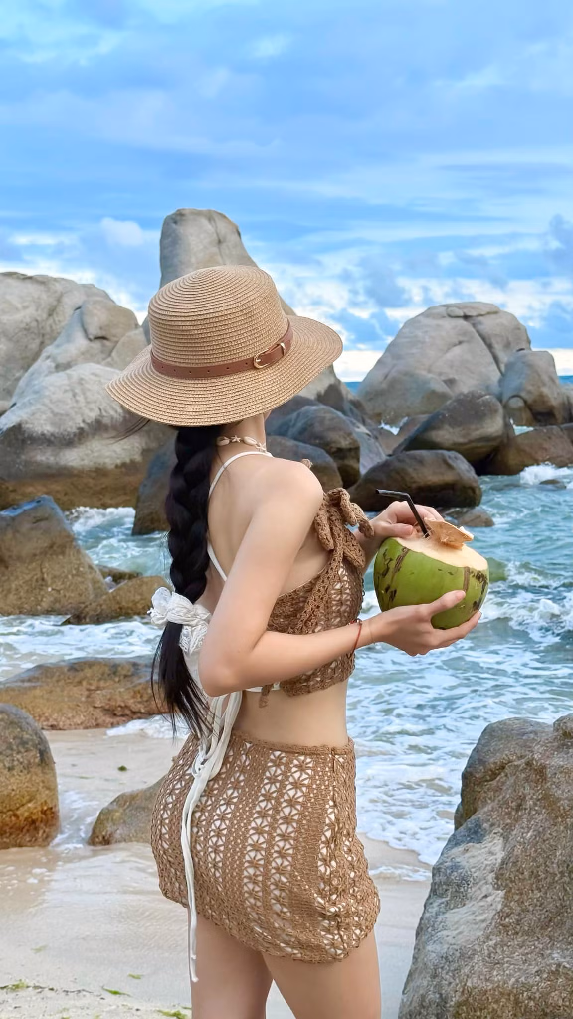 Không thể thiếu chiếc mũ cói rộng vành – phụ kiện “quốc dân” cho mọi cô nàng đi biển, vừa che nắng vừa tăng điểm thời trang. Dây vỏ sò đeo cổ và trái dừa tươi trên tay như hoàn thiện nốt bức tranh “nàng thơ mùa hè”.
