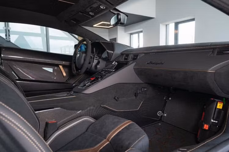Mở cửa bước vào trong khoang lái, chiếc xe giới hạn Lamborghini Aventador SVJ63 này có logo SVJ63 ở bậc cửa như là 1 dấu hiệu nhận biết rõ ràng so với 900 chiếc Lamborghini Aventador SVJ tiêu chuẩn. Nội thất xe có tông màu tối với điểm nhấn là sọc chữ Y chạy dọc ghế ngồi hay thảm sàn hoàn thành màu vàng hồng.