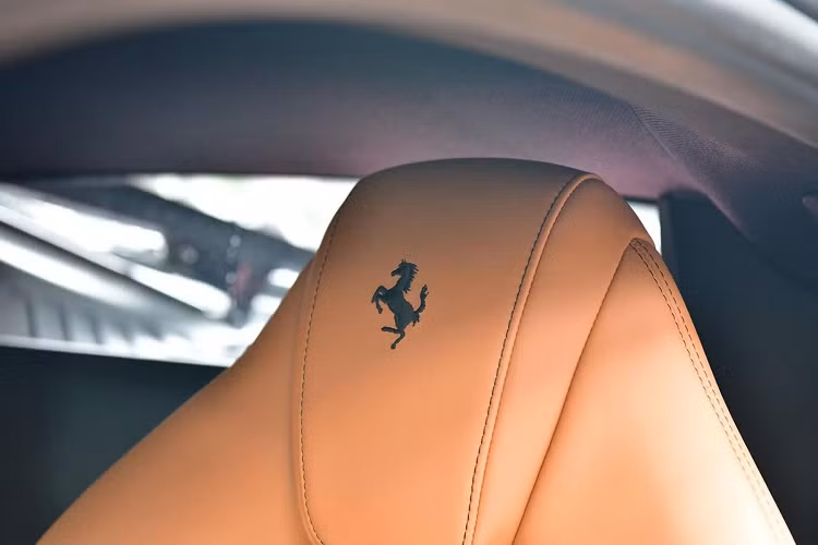 Bên trong khoang lái chiếc siêu xe Ferrari F8 Tributo màu đen đang được chào bán có nội thất bọc màu da bò cùng với các chi tiết bằng nhôm hay carbon, trên tựa đầu ghế ngồi của xe có logo ngựa chồm được thêu bằng chỉ đen, tạo đối lập với bộ ghế màu da bò.