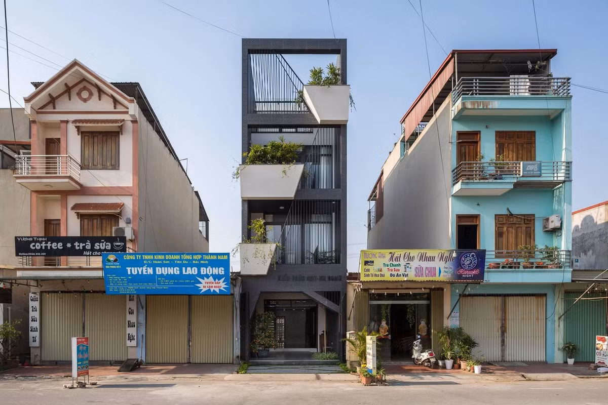 Sử dụng màu sơn ngoại thất màu đen khói và các nan sắt cùng màu làm mặt tiền cho căn nhà ống bị kẹp giữa nhiều ngôi nhà khác là một thiết kế được khá nhiều người ưa chuộng trong năm 2021. Điểm nhấn của thiết kế này là tạo ra các khối bê tông có hình chậu cây với kích thước và vị trí khác nhau ở mỗi tầng, sơn nó màu trắng rồi trồng cây xanh ở mặt tiền ngôi nhà, tạo ra điểm nhấn giữa một tổng thể màu đen.