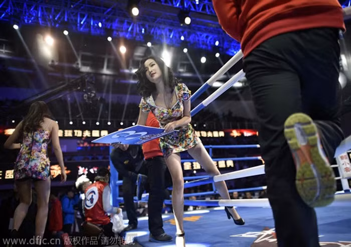 Liu Rongqing, cô gái 21 tuổi, chui qua dây thừng quanh võ đài cùng tấm biển sau khi bước quanh võ đài để báo số hiệp của trận đấu. Vốn là người mẫu chuyên nghiệp, Liu nói rằng, để làm thêm trong các trận đấu võ, các ứng cử viên phải có chiều cao 165-175 cm. Nhưng kỹ năng khó nhất là bước trên những đôi giày có gót 10 cm.