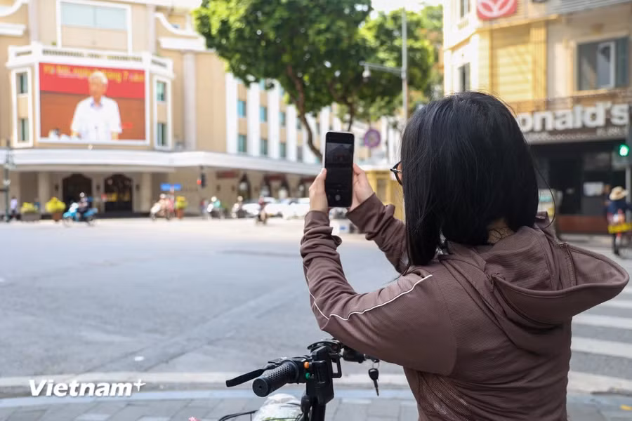 Một người dân đang đứng ghi lại hình ảnh của Tổng Bí thư Nguyễn Phú Trọng trên tấm màn LeD của một trung tâm thương mại phố Tràng Tiền. (Ảnh: Minh Hiếu/vietnam+)
