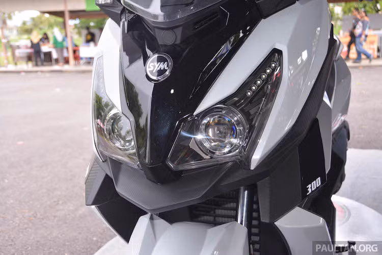 So với bản concept, SYM CruiSYM 300i đã có khá nhiều sự thay đổi. Ở phía trước, cũng giống như MAXSYM 500, CruiSYM 300i cũng sở hữu cặp đèn pha kép với 2 bóng pha dạng thấu kính projector và đèn chiếu sáng ban ngày LED. Tuy nhiên so với MAXSYM, cụm đèn pha của xe đã có thiết kế khá khác biệt với kích thước to hơn, nhưng ít sắc sảo hơn.