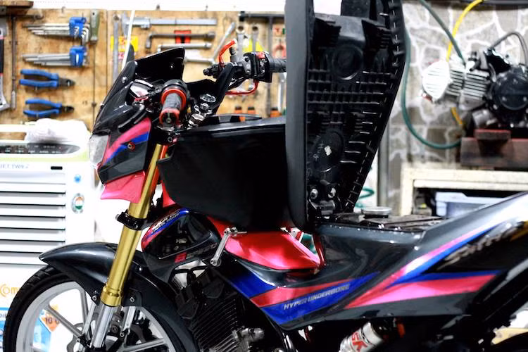 Với kiểu dáng hyper underbone và thiết kế cũ chưa có hộc đồ ở lườn như Raider 150 Fi đời mới, Satria 150 nguyên bản vốn hoàn toàn không có bất kỳ một hộc chứa đồ nào. Để khắc phục nhược điểm này, chủ xe đã trang bị một hộp đồ bằng nhựa nằm giữa lườn.
