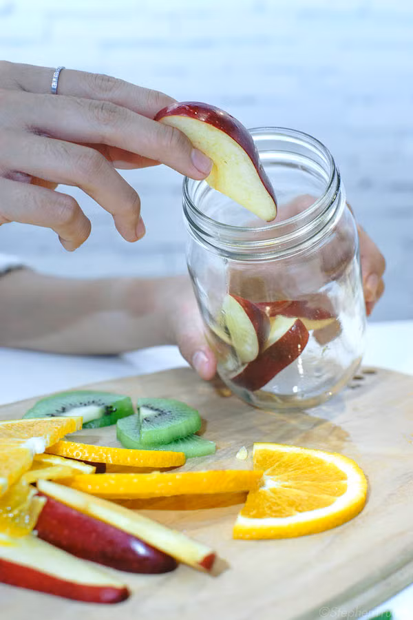 Công thức detox từ táo, kiwi và chanh Tây. Nguyên liệu: ½ quả táo, ½ quả chanh tây (vàng), ½ quả kiwi, 2 khoanh cam Mỹ. Táo sau khi rửa thật sạch, bạn cắt táo làm đôi, bỏ đi phần lõi bên trong rồi cắt thành từng múi dày khoảng 1cm. Chanh tây bạn cũng cắt thành từng khoanh mỏng khoảng 0,5cm, nhớ không được bỏ vỏ. Kiwi bỏ vỏ và cắt thành từng miếng mỏng. Bỏ hết táo, cam, chanh tây, kiwi vào hũ rồi thêm nước vào để trong tủ lạnh chờ khoảng 2 - 3 giờ đồng hồ thì có thể lấy ra dùng.