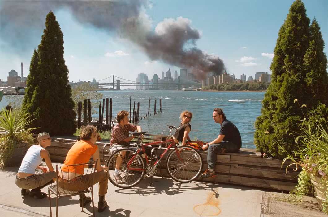Các thanh niên tán gẫu trong công viên ở khu Brooklyn, phía xa là cột khói từ tòa nhà WTC, một bức ảnh gây nhiều tranh cãi về vụ 11/9. Ảnh: Thomas Hoepker/ Magnum Photos.