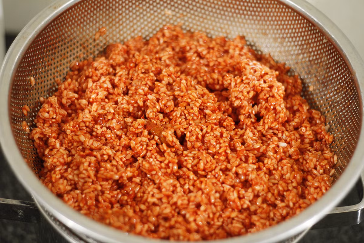 Trộn gạo nếp với thịt gấc, ở bước này, trộn đều tay để gạo ngấm đều màu đỏ từ gấc. Ảnh minh họa
