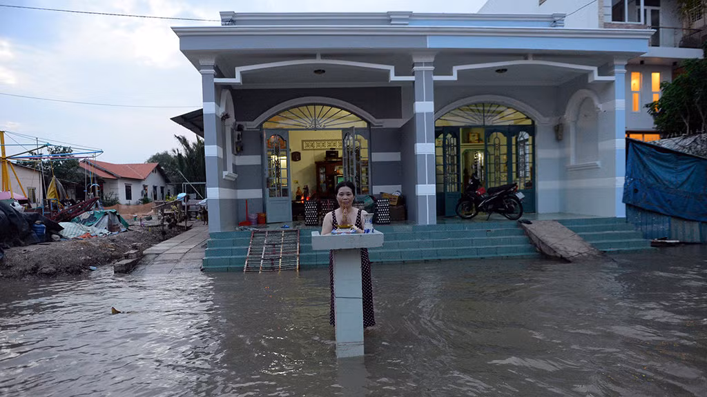 Một người phụ nữ thắp nhang giữa vùng nước mênh mông trước nhà ở Nhà Bè - Ảnh: HỮU KHOA